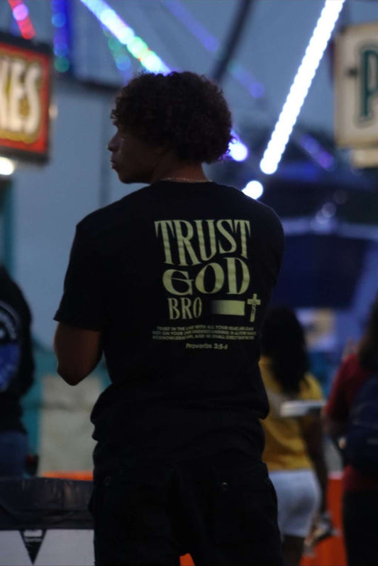 5'9 Model Wearing a black t-shirt with 'Trust God Bro' in a festive outdoor setting